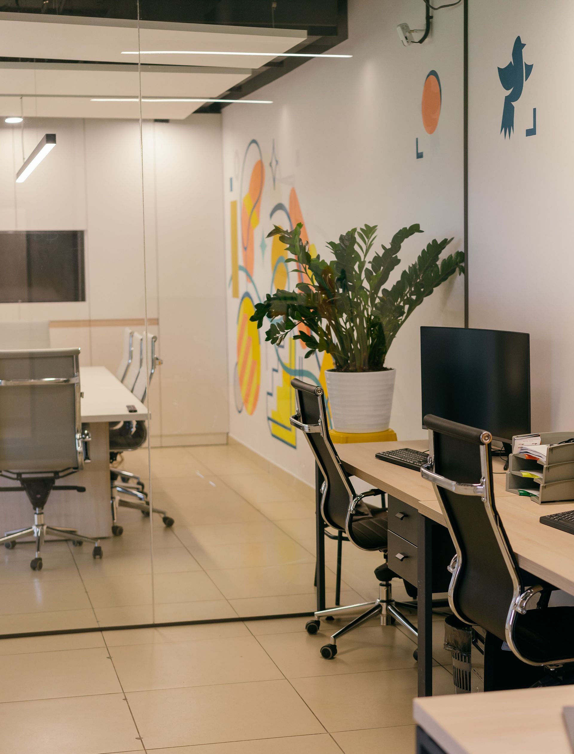 Spacious and contemporary office interior with glass partitions, stylish furniture, and vibrant wall art.
